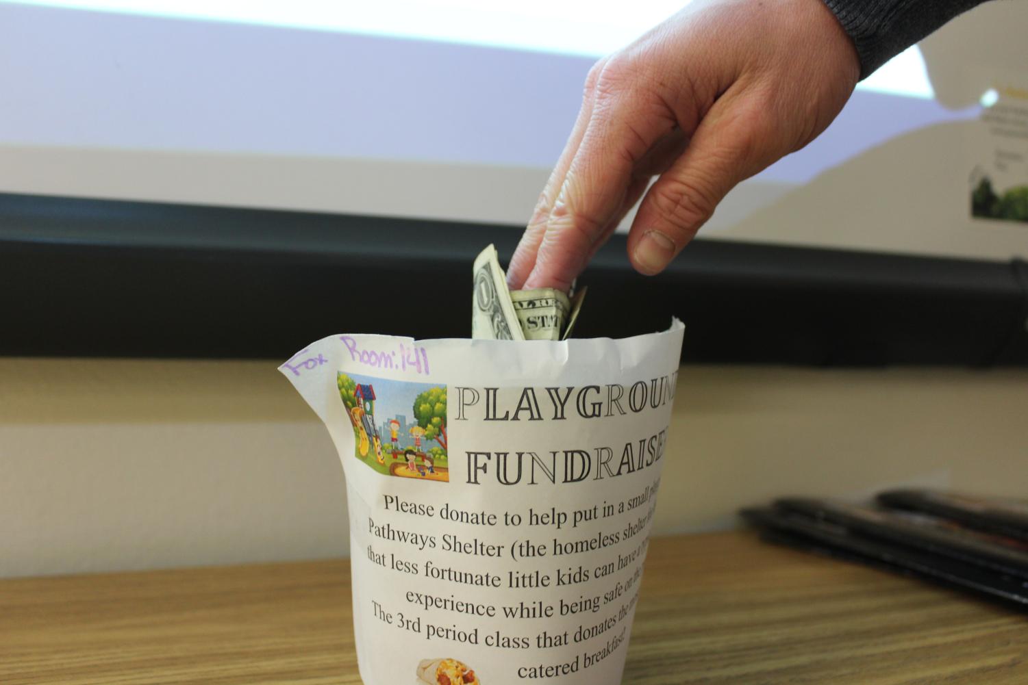 A student places money into one of the fundraiser buckets located throughout GJHS that will be used to build a playground at the Pathways Shelter. The fundraiser goes through Feb. 2.