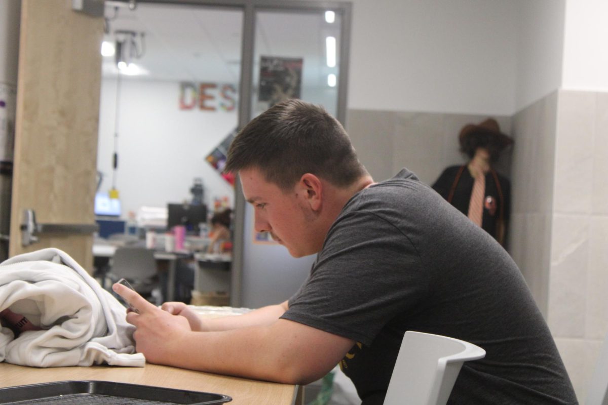 GJHS sophomore Cayden Olsen uses his phone while sitting outside of a classroom. Many students at GJHS find time to use their phones despite the bans.